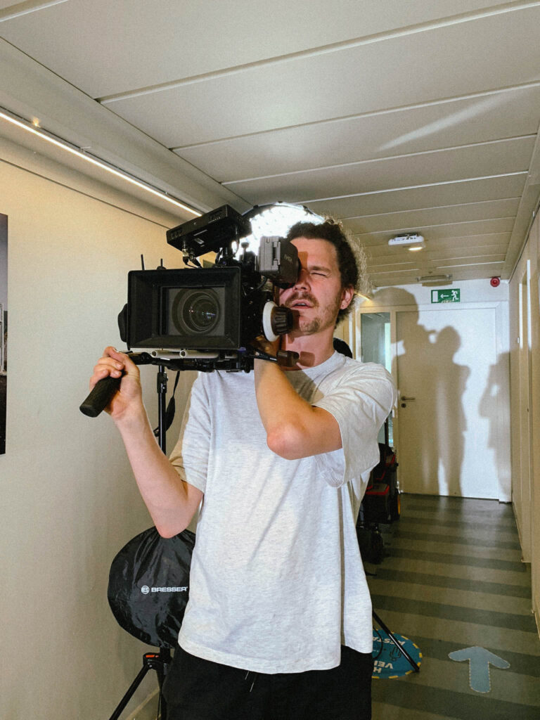 Cameraman Corneel met grote camera op schouder in een werkplaats, behind the scenes Equans
