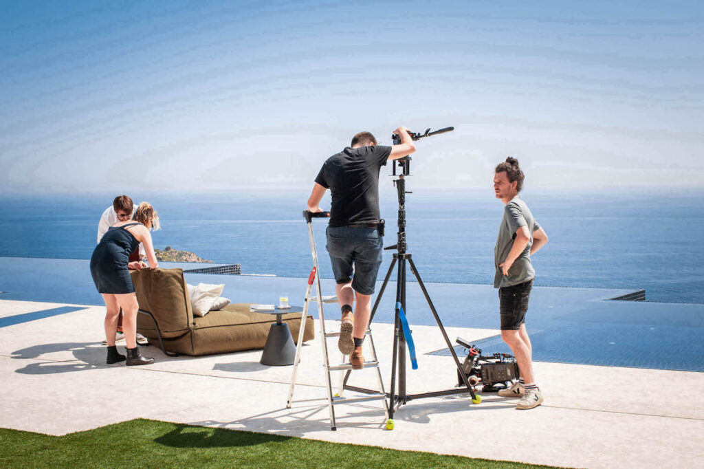 Cameraman met statief op terras met zeezicht, behind the scenes Fiqa Textiles
