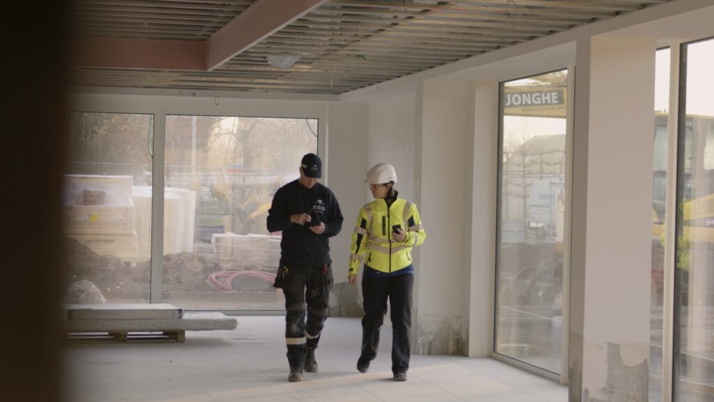 Twee EEG medewerkers in veiligheidsuitrusting lopen op een bouwwerf